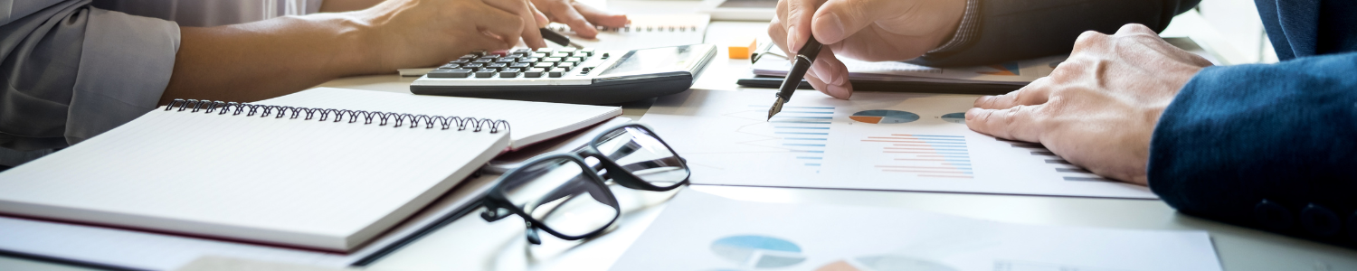 Itens de contabilidade em cima de uma mesa, com pessoas analisando dados em cadernos