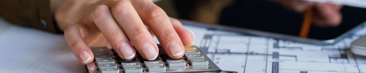 Mão digita em calculadora, com papéis ao fundo